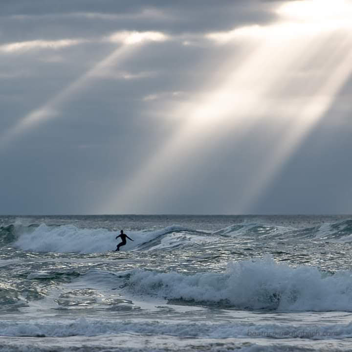 Un surfeur danse sur les vagues, sous des rayons de soleil perçant les nombreux nuages gris. Apprendre à danser sur les difficultés.