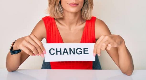 Une femme blonde habillé d'un top rouge présente une affichette où est inscrit le mot "change"